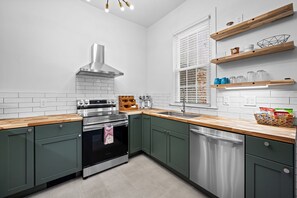 Eine moderne Küche mit Edelstahlgeräten, grünen Schränken, Holzarbeitsplatten und eingebauten Regalen.