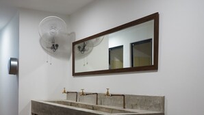 Une salle de bain avec un lavabo en marbre, un miroir, un ventilateur et une poubelle.