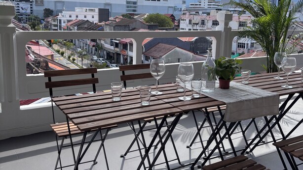 Un balcon avec une table dressée pour le dîner, d’où l’on peut admirer un paysage urbain avec des bâtiments et une montagne à l’horizon.
