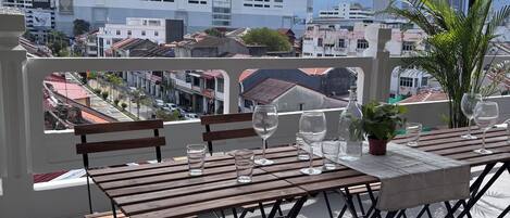 A balcony with a table set for dining, overlooking a cityscape with buildings and a mountain in the distance.