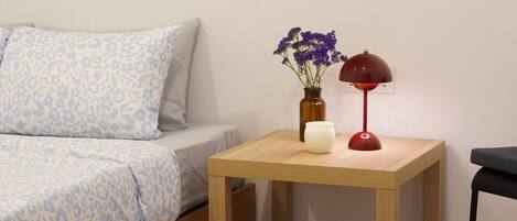 Un dormitorio con una cama, una mesita de noche con un florero, una lámpara roja y un reloj de pared.