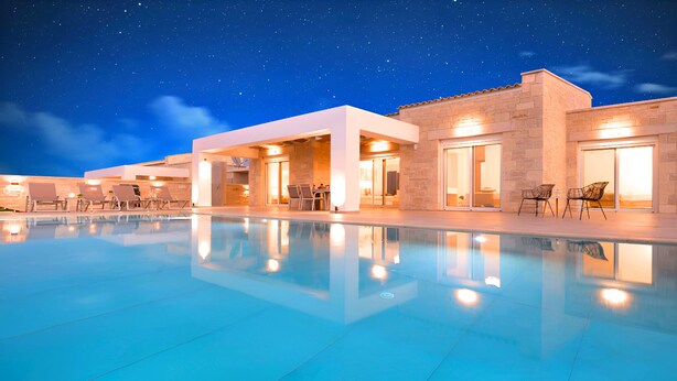 Zona de piscina amb un cel nocturn estrellat, una piscina i un edifici amb diverses portes i finestres.
