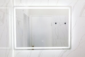 A bathroom with a white door, a mirror with a white frame, and marble-patterned walls. - The Kingston Vista Suite - Central Cozy 1-Bedroom Apt in Kingston with AC (Kingston)