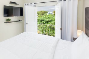 Une chambre d’hôtel avec un lit, un téléviseur fixé au mur, un balcon donnant sur un espace verdoyant et une porte menant à l’extérieur.