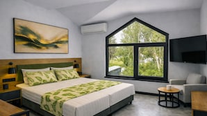 A modern bedroom with a large bed, a TV, a window with a view of trees, and a painting on the wall. - Raya Boutique (Sunny Beach)