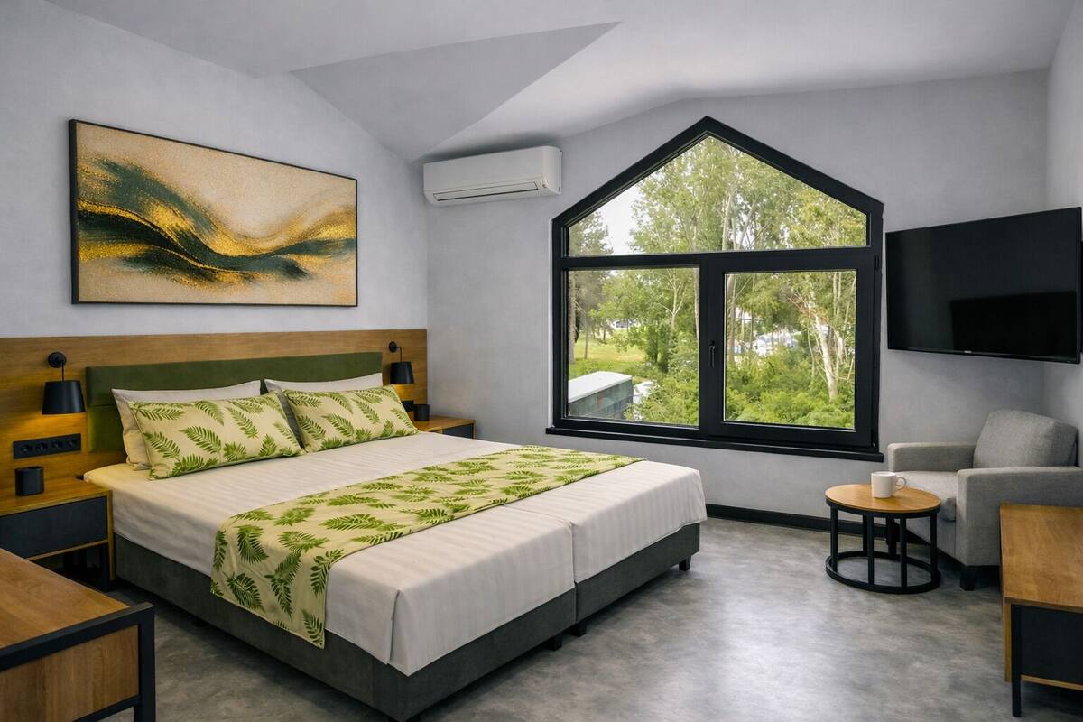 A modern bedroom with a large bed, a TV, a window with a view of trees, and a painting on the wall.