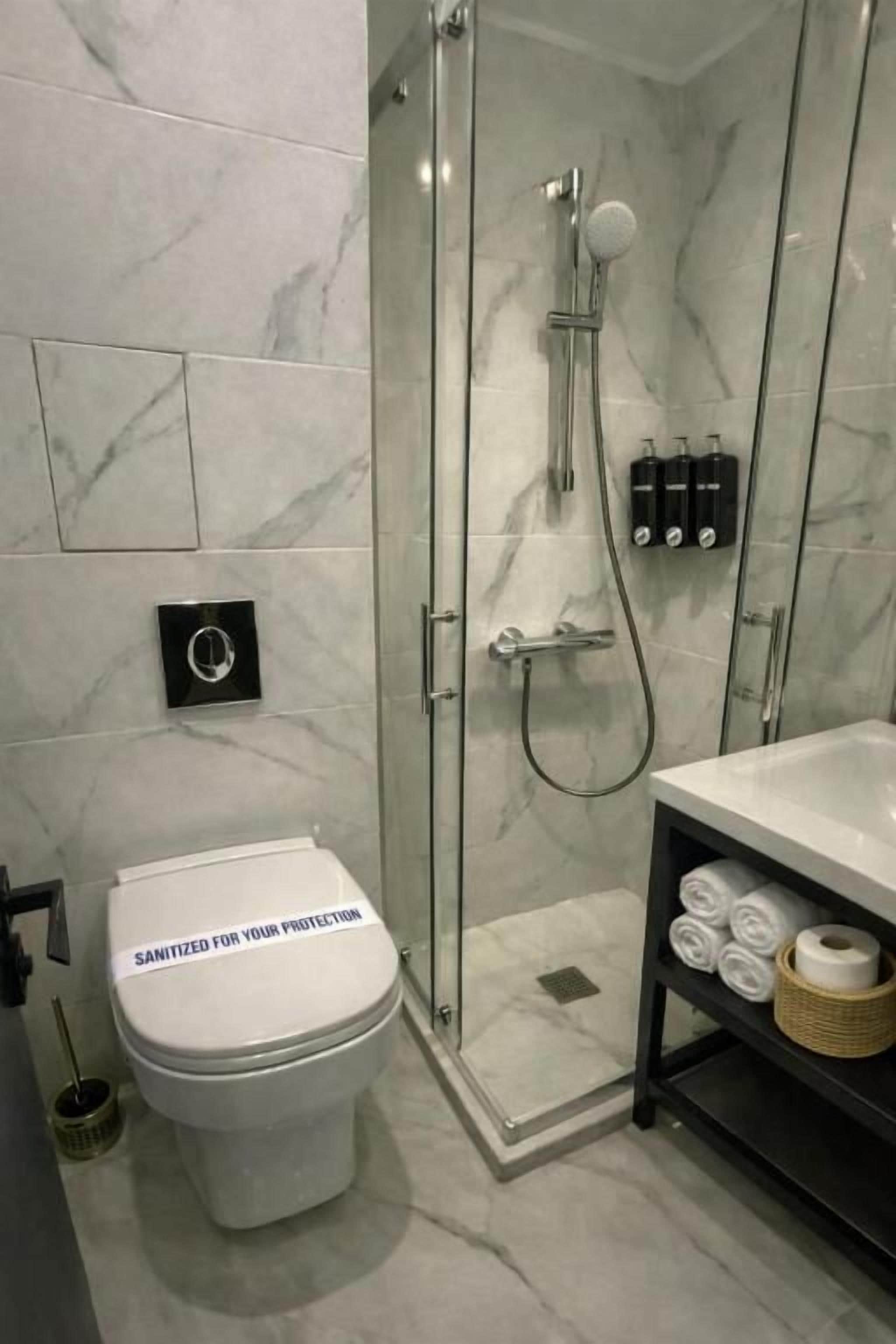A modern bathroom with a glass-enclosed shower, a toilet, and a shelf with toiletries.