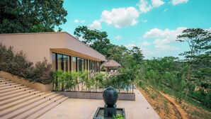 A modern building with a staircase leading to a thatched-roof structure, surrounded by lush greenery. - The 180 villa (Galle)