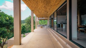 A covered outdoor area with a concrete floor, a wooden ceiling, and a view of a modern interior with a dining area. - The 180 villa (Galle)