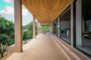 Un espacio al aire libre techado con piso de concreto, techo de madera y vista de un interior moderno con zona de comedor.