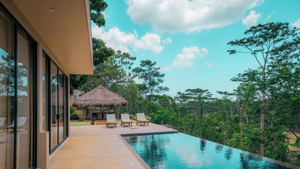A modern building with a swimming pool, lounge chairs, and a thatched-roof structure. - The 180 villa (Galle)