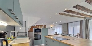 A modern kitchen with a central island, built-in oven, and a dining area with a long table. - Comfortable group gite ideally located in Brittany. Pets welcome (Mellé)