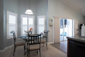 A dining area with a round table and four chairs, a hanging light fixture, and a view through a glass door to the outside. - Pelicans Landing - Three Bedroom House, Sleeps 6 (Davenport)