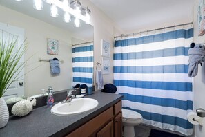 A bathroom with a striped shower curtain, a sink with a mirror, and a toilet. - Pelicans Landing - Three Bedroom House, Sleeps 6 (Davenport)