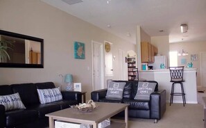 A living room with a black leather sofa, a coffee table, and a kitchen area in the background. - Sunset Ridge Villa - Five Bedroom House, Sleeps 10 (Davenport)