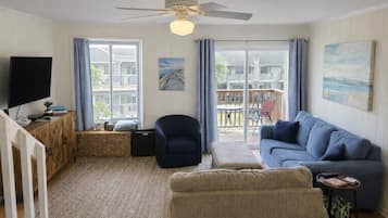 A living room with a TV, sofa, armchair, and a ceiling fan.