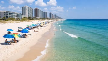 A beach with rows of umbrellas, a sandy shore, and high-rise buildings in the background.