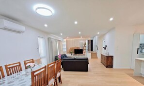 Een moderne woonkamer met een bank, televisie en een eetgedeelte met stoelen en een tafel.