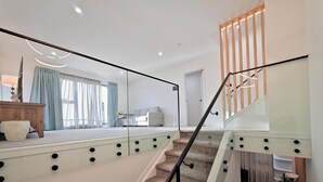 Una escalera moderna con barandillas de cristal y una barandilla de madera, que conduce a una habitación con un ventanal grande, un sofá y una mesa.