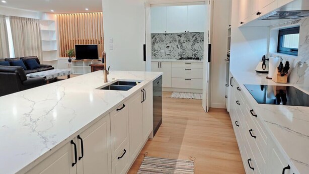 Una cocina moderna con armarios blancos, encimera de mármol y estufa integrada.