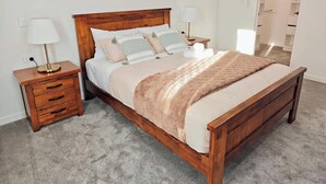 Un dormitorio con cama de madera, dos mesitas de noche con lámparas, suelo alfombrado y un armario con puerta.