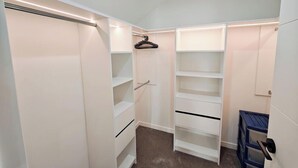 Un vestidor con estantes abiertos, barra para colgar y un armario azul.