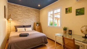 Una camera da letto con parete a mattoni, un letto con testiera, una scrivania con sedia e una finestra vista su del verde.