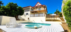 Ein zweistöckiges Gebäude mit Pool, einer Holzterrasse und einer überdachten Außenbereich-Sitzgelegenheit.