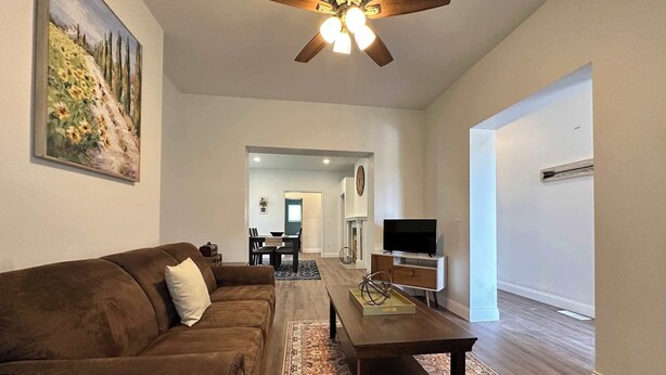 A living room with a brown sofa, a coffee table, a TV on a stand, and a ceiling fan. - Beautiful 2 Bedroom Apartment - Easy City Access (Pittsburgh)