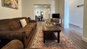 A living room with a brown sofa, a coffee table, a television on a stand, and a painting on the wall. - Beautiful 2 Bedroom Apartment - Easy City Access (Pittsburgh)