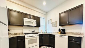 A kitchen with dark cabinets, a white stove, a microwave, and a dishwasher. - Beautiful 2 Bedroom Apartment - Easy City Access (Pittsburgh)