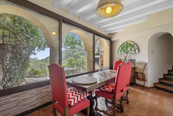 A dining area with a table, chairs, and large windows offering a view of greenery.
