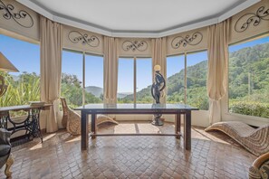 A room with a large table, chairs, and a view of a mountainous landscape through large windows.