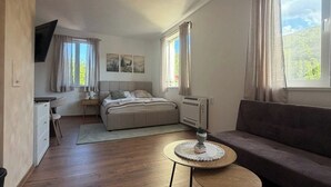 A modern, well-lit room with a bed, a sofa, a small table, and a TV.