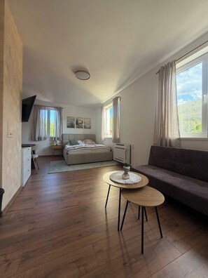 Una habitación moderna y luminosa con una cama, un sofá, una mesita y un televisor.