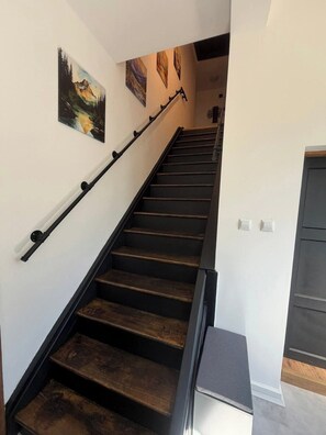 Un escalier avec des marches en bois et des rampes noires, menant à un palier avec une porte.