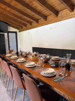 Una larga mesa de comedor dispuesta con platos, vasos y cubiertos, rodeada de sillas.