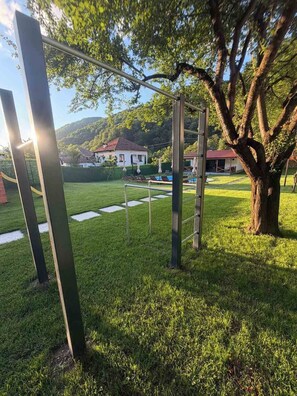 Un espacio al aire libre con césped, estructuras metálicas, un árbol y una casa al fondo.