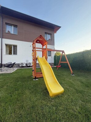 Una casa con un'area giochi in legno nel cortile, comprensiva di scivolo.