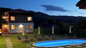 A two-story house with a swimming pool, surrounded by a well-maintained lawn and stone pathways.