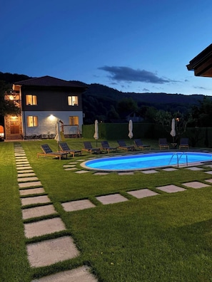 Una casa de dos plantas con piscina, rodeada de césped cuidado y senderos de piedra.