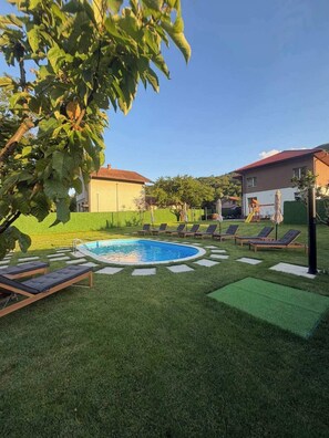 En trädgård med en pool, solstolar och en välskött gräsmatta.