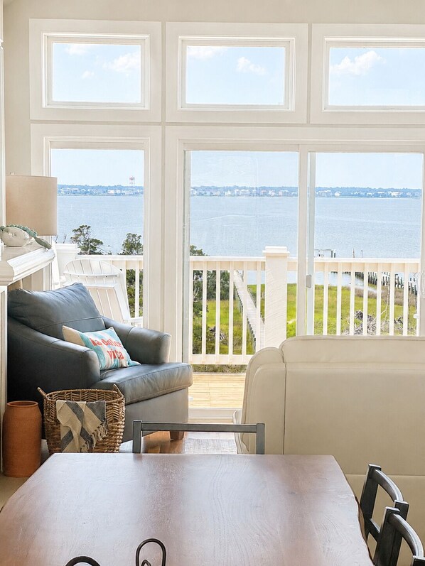 A room with a view of the water, a sofa, a table, and a lamp.