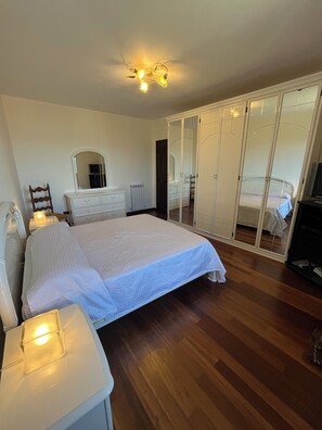 A bedroom with a bed, dresser, mirror, wardrobe, and bedside lamp.