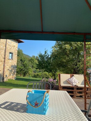 A covered outdoor seating area with a table, a blue bag, and a wooden bench with cushions.