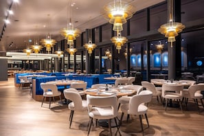 Ein Restaurant mit mehreren Tischen, Stühlen und hängenden Pendelleuchten.
