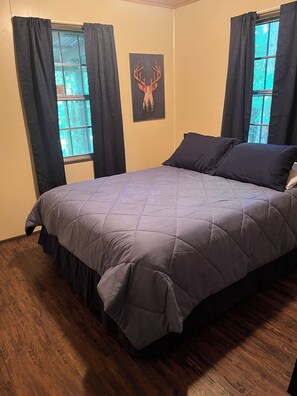 Ein Schlafzimmer mit einem Bett, zwei mit Vorhängen versehenen Fenstern, einem Wandbild eines Hirschgeweihs und Holzböden.