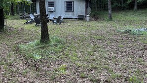 A rustic cabin with a porch, surrounded by trees and a grassy area.
