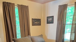A bedroom with a bed, curtains, a framed picture, and a wooden floor.