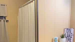 A bathroom with a shower curtain, toilet, wooden floor, and a cabinet.